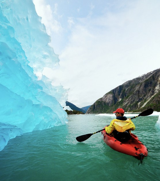 A kayaker paddling past a towering blue iceberg