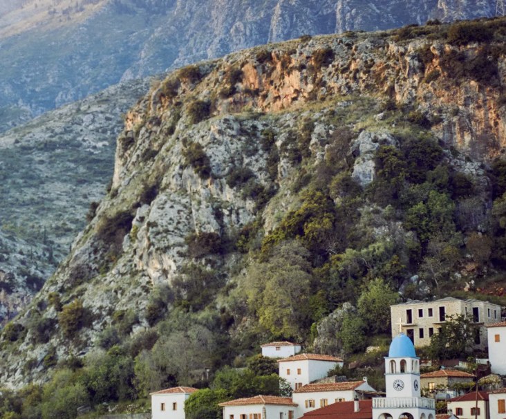 A white village with a blue-domed clock tower beneath rugged mountains